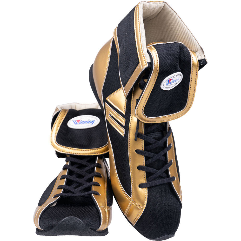 A pair of boxing boots in black and metallic gold, featuring a lace-up front, high ankle support, and a visible 'Venum' brand logo patch on the ankle strap.