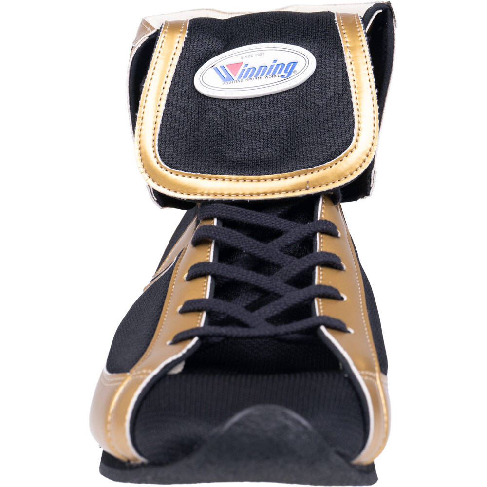 A close-up of a boxing glove from the front showing the black and gold fabric construction, black laces, and the oval Winning brand patch on the top strap.