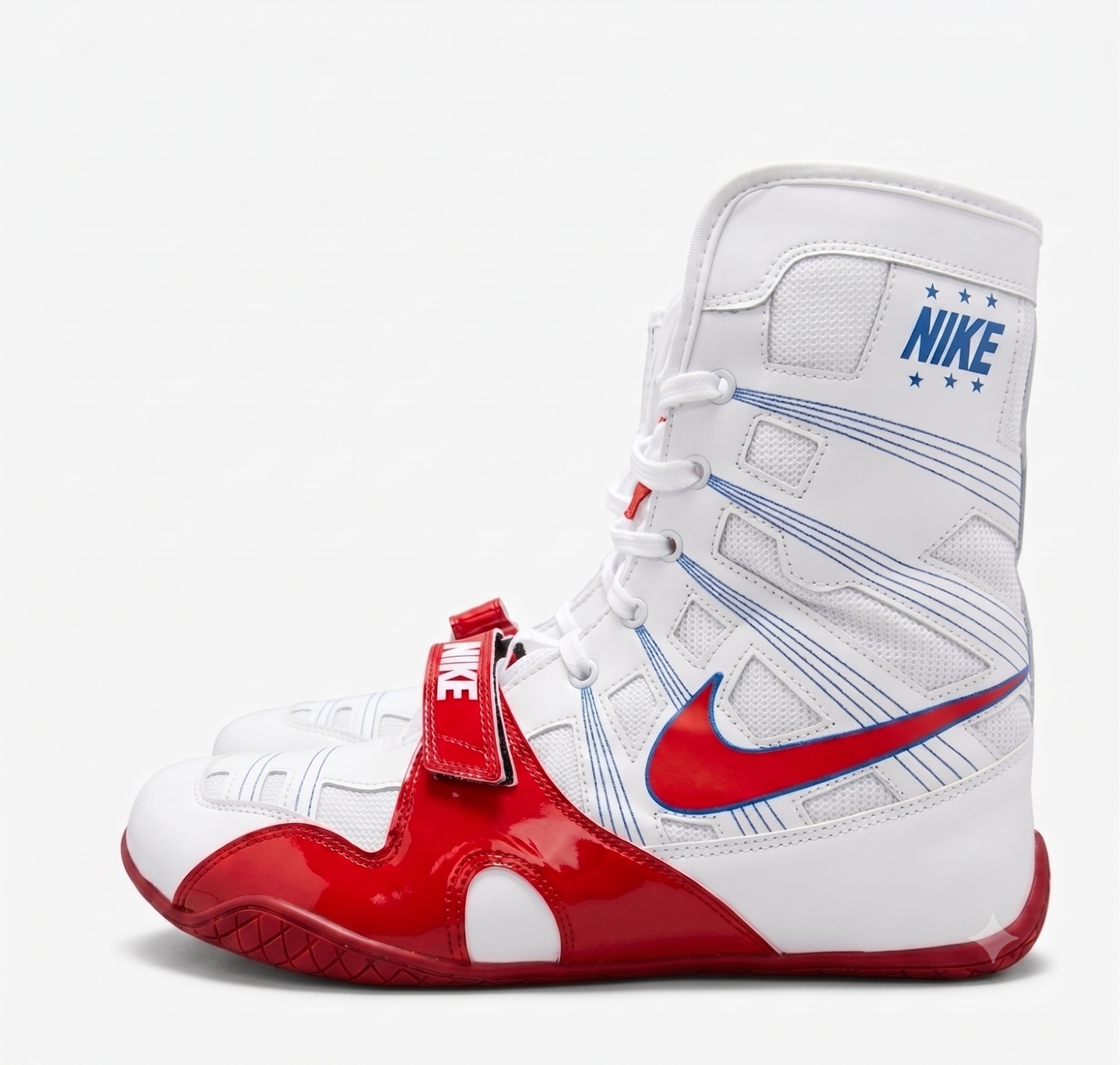 A high-top Nike boxing shoe in white, red, and blue, featuring a red swoosh, a red strap with a white Nike logo, and a red outsole, shown against a light gray background.